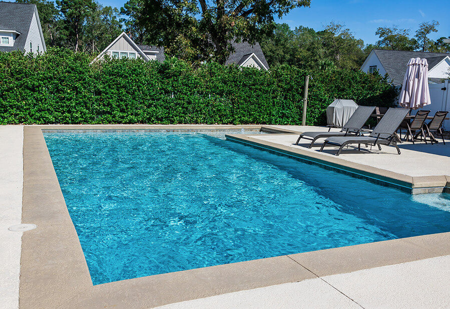 A serene backyard pool surrounded by lush greenery, featuring lounge chairs and a sunshade, ideal for relaxation and leisure.