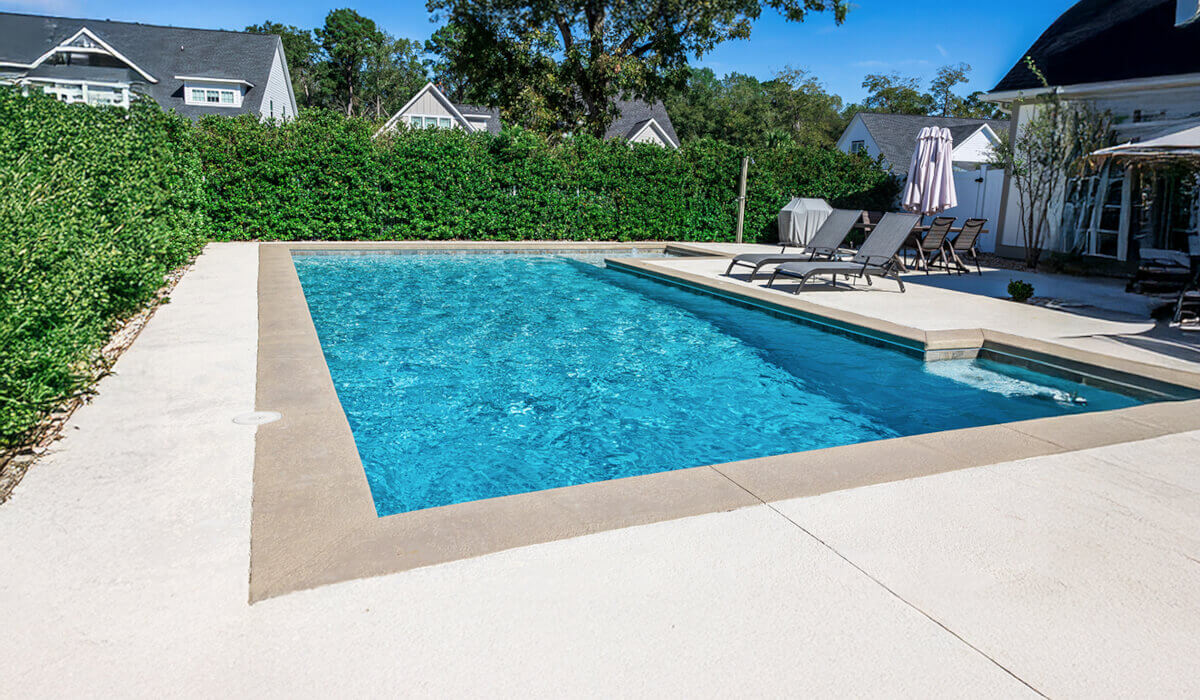 A serene backyard pool surrounded by lush greenery, featuring lounge chairs and a sunshade, ideal for relaxation and leisure.