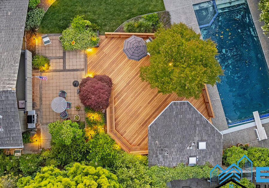 Aerial view of a spacious backyard featuring a wooden deck, landscaped garden, seating area, and a swimming pool.