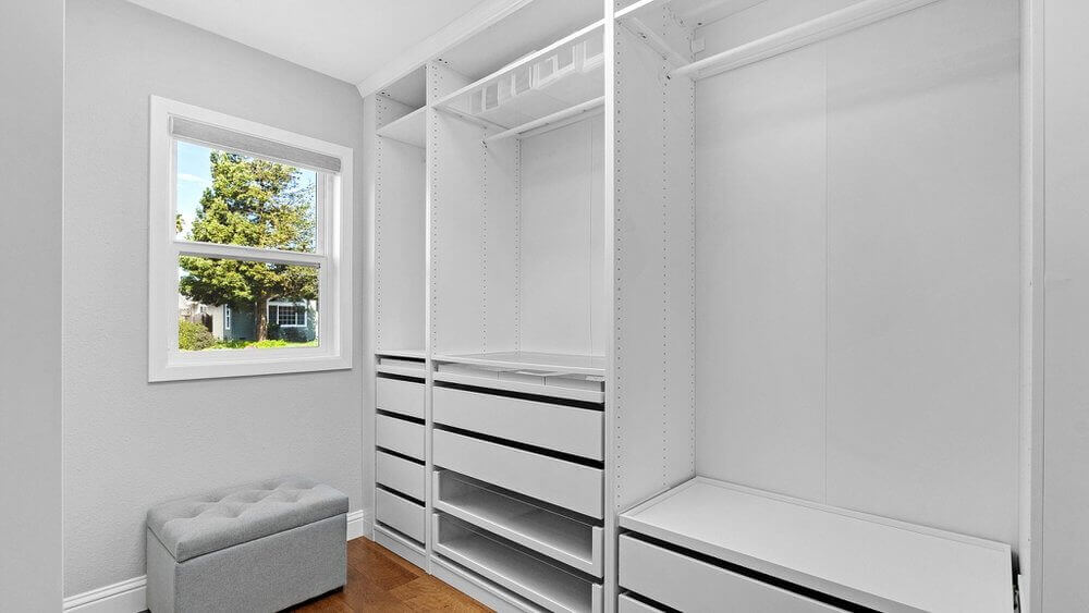 A closet with white shelves and storage space. There is a window overlooking the backyard.